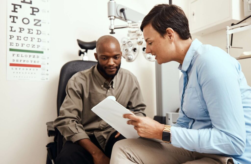 An optometrist shows her patient a clipboard to discuss the results of his eye exam.