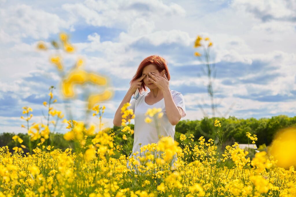 A woman rubbing her eyes outside at the park suffering from allergies