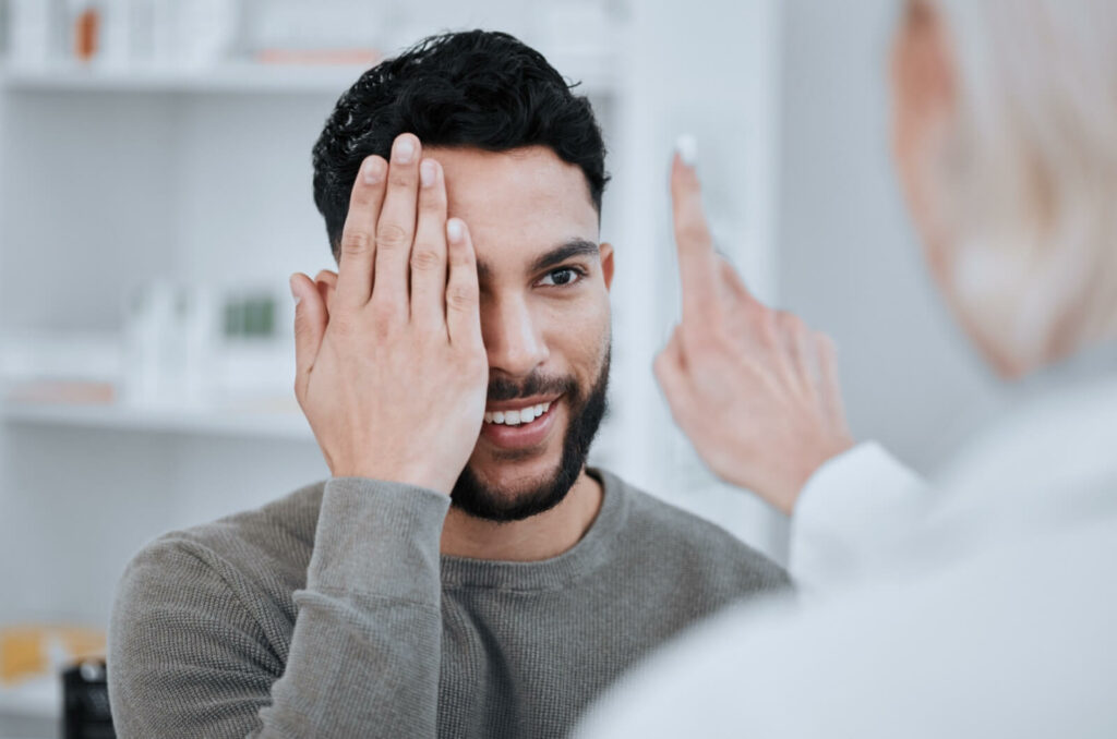 A patient covers one eye with a hand to follow their optometrist's finger with a single eye