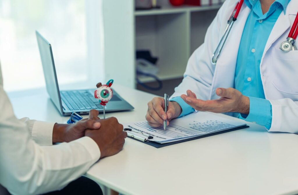 A close-up image of an eye doctor writing on a clip board and discussing diagnosis with a patient.