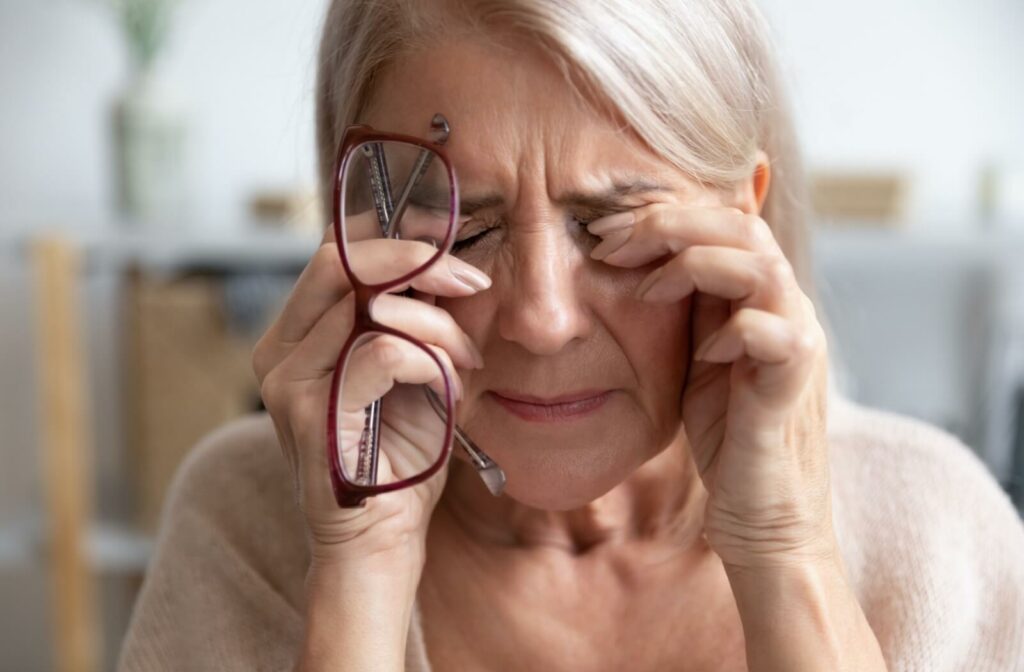 A person rubs their burning eyes after crying, holding their glasses in their right hand.