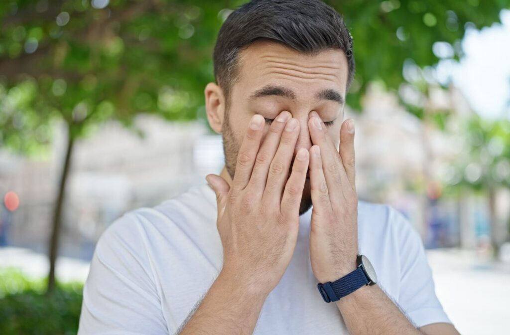 A person rubs their burning eyes while outdoors.