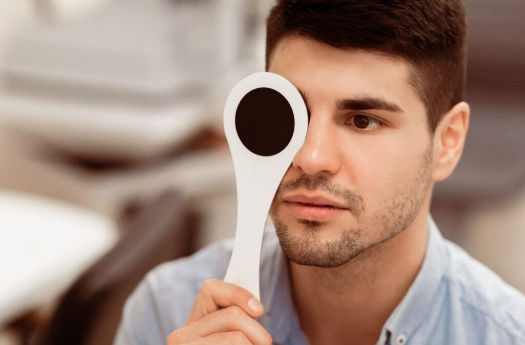 Person holding occluder over one eye during a routine vision exam at the optometrist’s office.