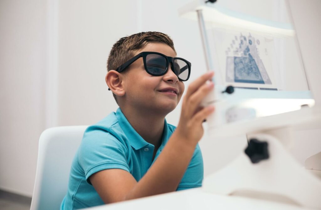 A smiling child with dark glasses undergoes vision therapy.