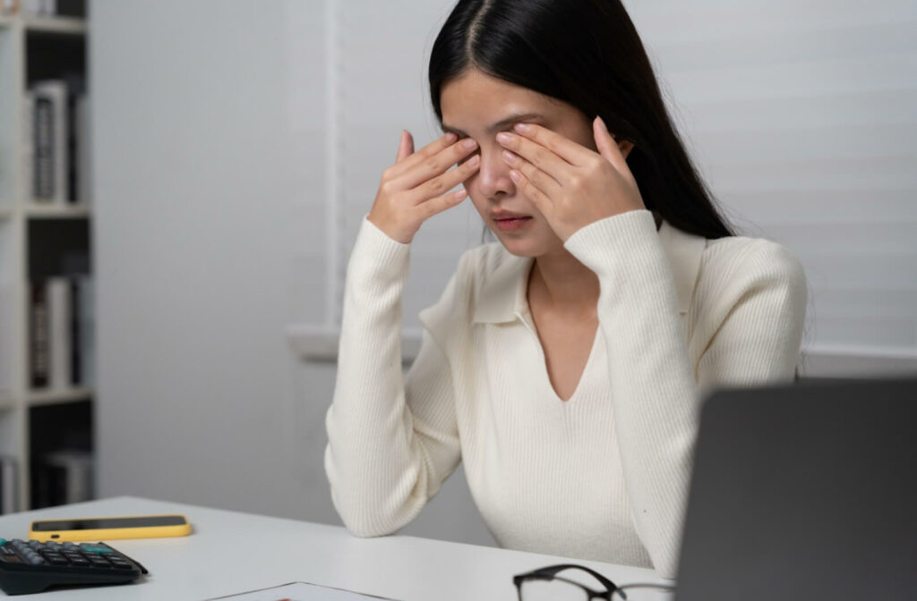 Woman rubbing her eyes in front of a laptop, showing signs of digital eye strain or fatigue.