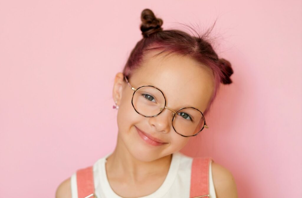 A child smiling while wearing a pair of round, gold-rimmed eyeglasses.