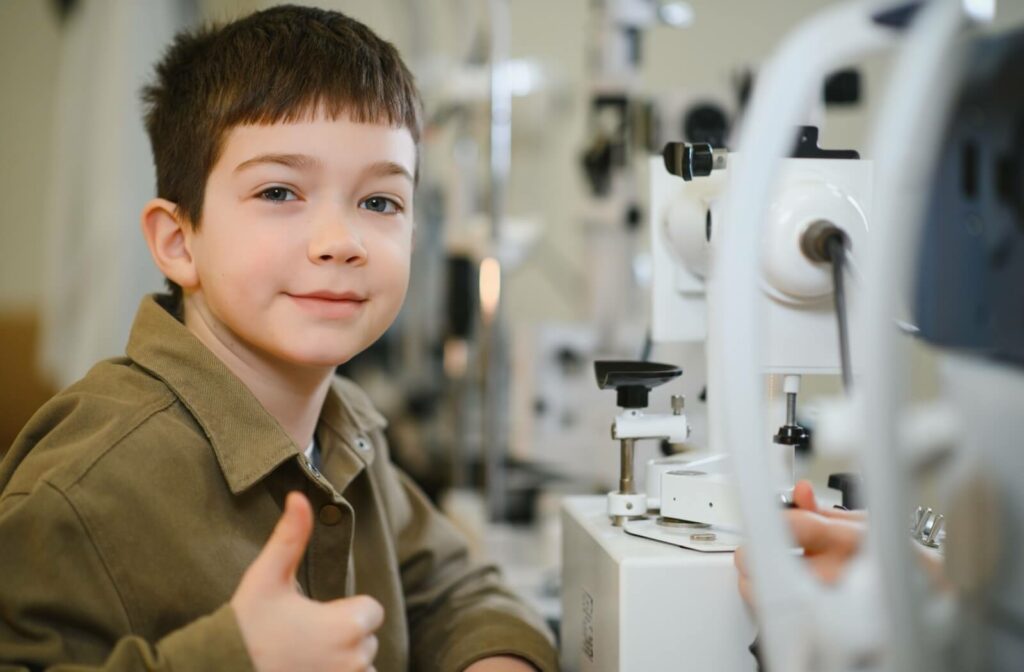 A child giving a thumbs up while sitting next to professional vision therapy equipment.